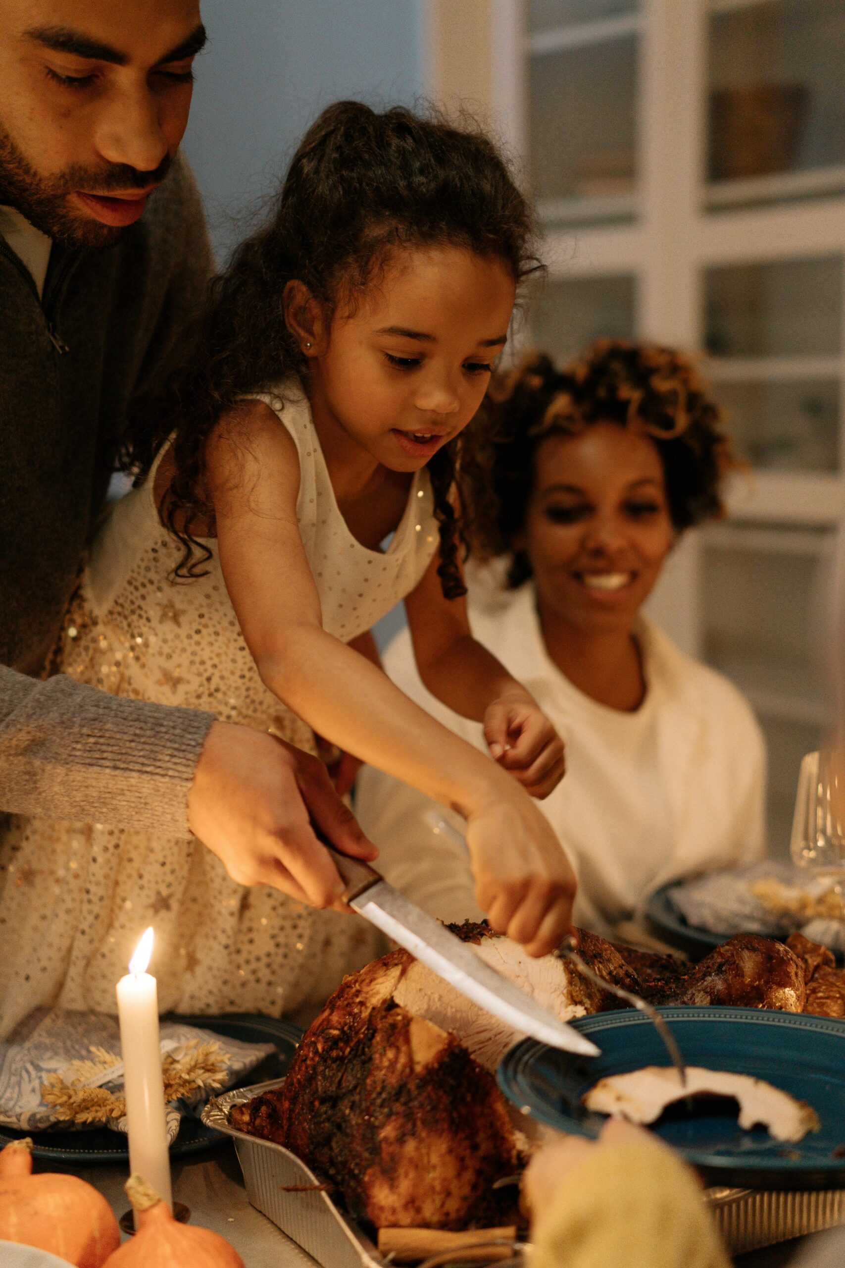 A warm family gathering around the table slicing a turkey for Thanksgiving dinner.