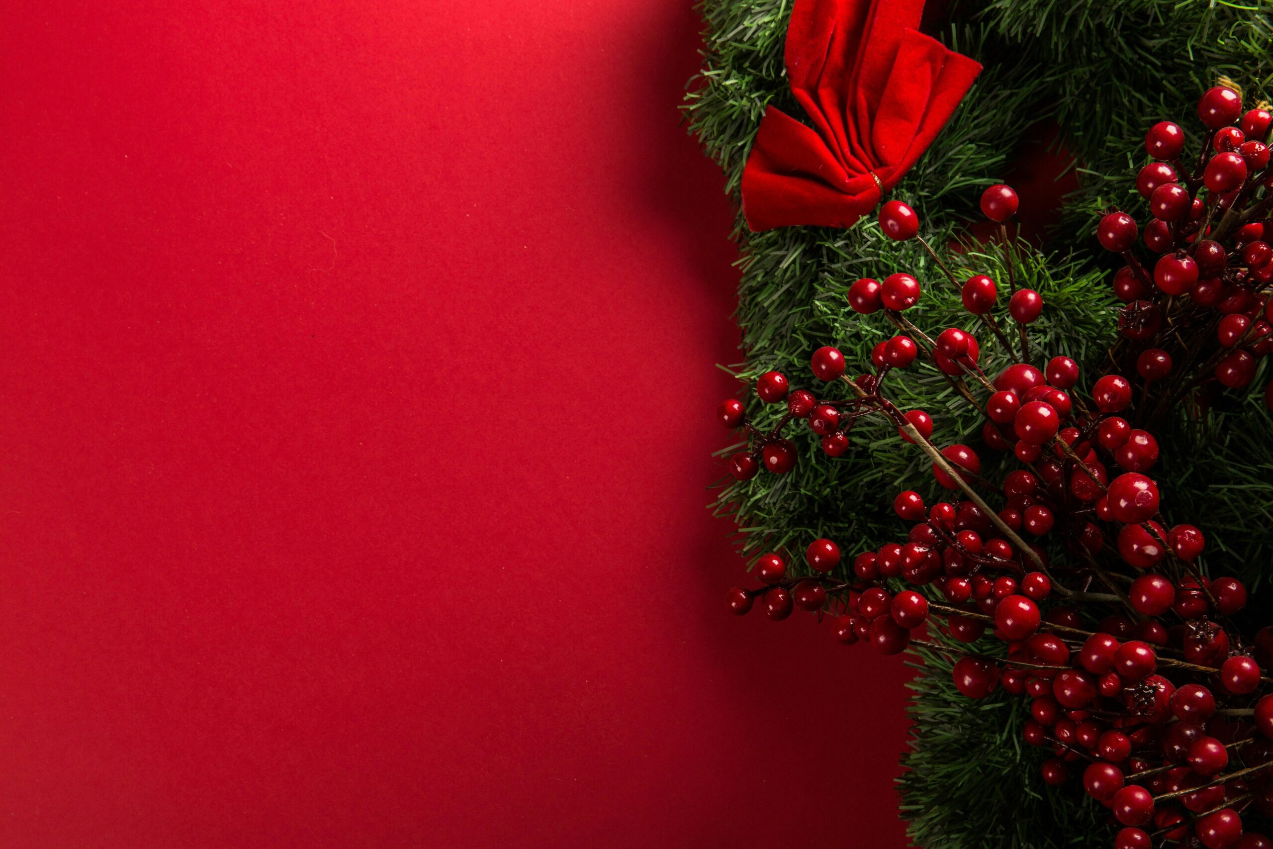 A vibrant Christmas wreath with red berries and bow on a red background.